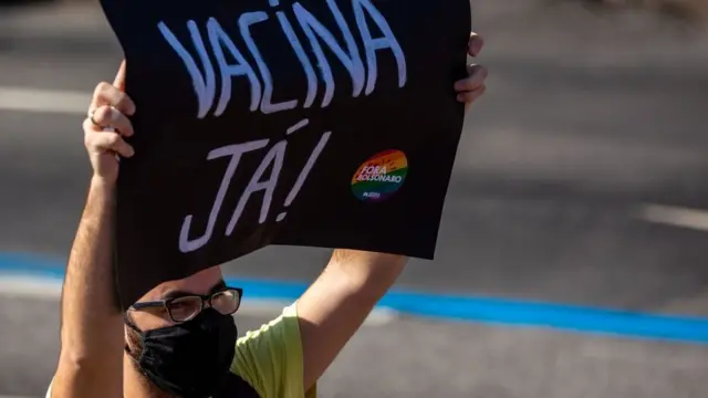 Manifestante segura cartaz onde se lê 'vacina já'