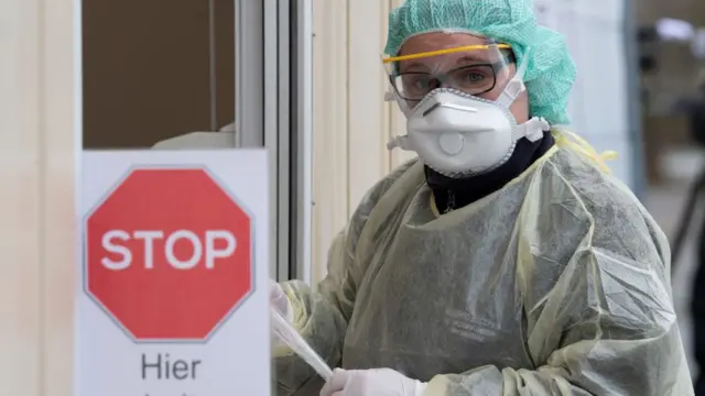Una mujer con una mascarilla y un letrero de "Detenerse"