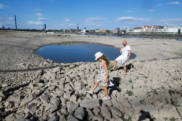A family walks next to a puddle in the partially dried riverbed of Rhine, in front of the skyline of Dusseldorf, Germany