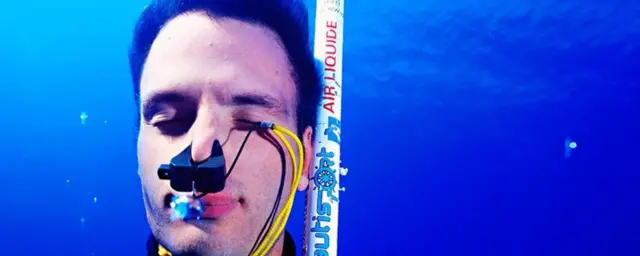 นักดำน้ำแบบตัวเปล่าคนหนึ่งกำลังดำลงใต้น้ำโดยใช้ไม้ค้ำขนาดเล็กช่วยนำทาง