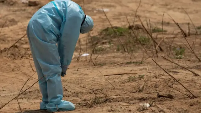 Un travailleur de la santé réagit dans un cimetière en Inde avant des funérailles