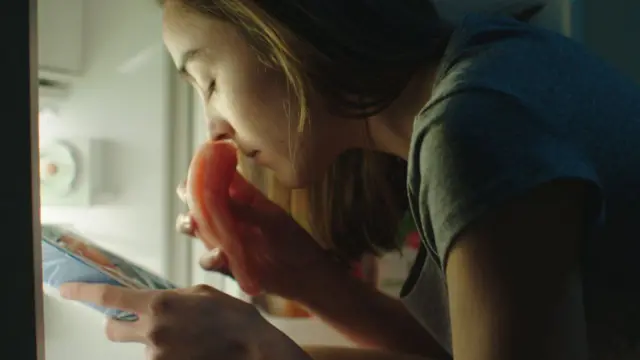 Un fotograma de la película en el que aparece la protagonista oliendo un pedazo de pollo crudo frente a la nevera.