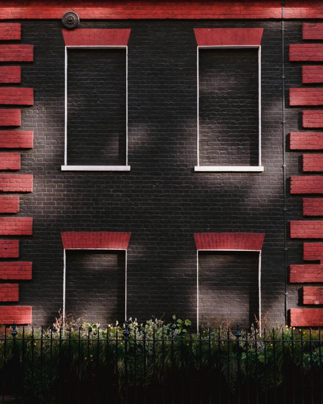 Four blocked windows on a building painted black and red, on Davies Street, London