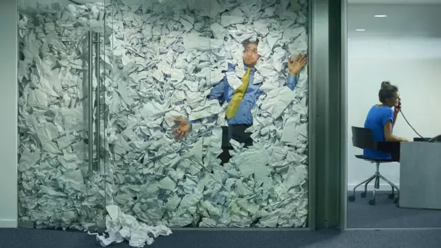 Hombre atrapado en un cubículo lleno de papeles