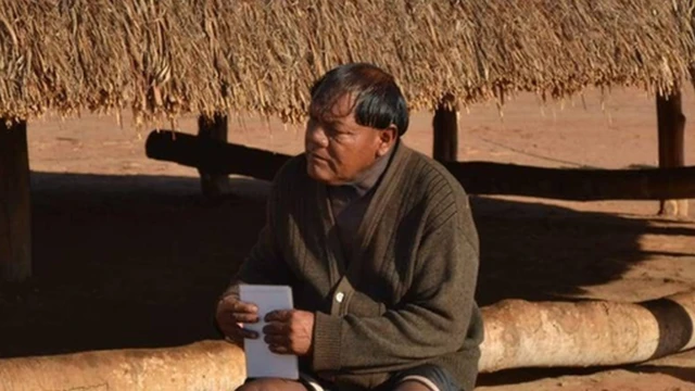 Aritana Yawalapiti, líder do Alto Xingu, sentadobetboo üye olfrente a uma construção tradicional