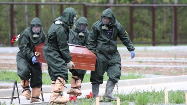 Pessoas carregam caixão usando roupas protetoras na Rússia