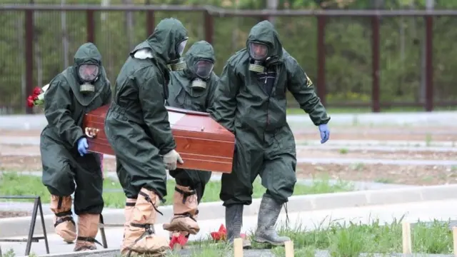 Pessoas carregam caixão usando roupas protetoras na Rússia