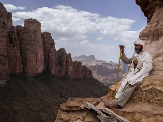 An elderly man leans on rocks and looks at the mountainous landscape