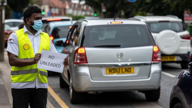 A Shell garage employee holds a sign on the side of the road informing a queue of traffic that they do not have unleaded petrol on September 25, 2021 in Blackheath, London, United Kingdom.