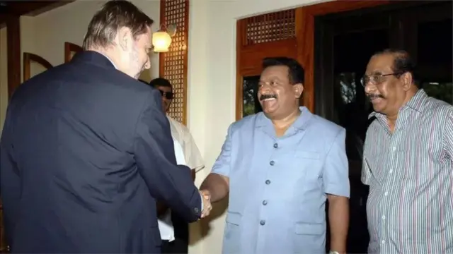 નૉર્વેના વિદેશમંત્રી જૉન પીટરસન સાથે હાથ મેળવતા પ્રભાકરન, સાથે બાલાસિંઘમ (ચસવીર 11 નવેમ્બર 2004ની છે)