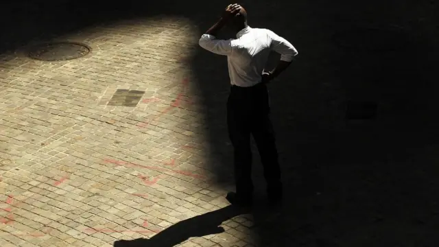 Un hombre con expresión abatida, cuya sombra se proyecta en el piso, en claroscuro