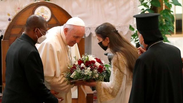 بغداد – فتاة تقدم باقة ورود إلى البابا فرنسيس في كنيسة سيدة النجاة في بغداد