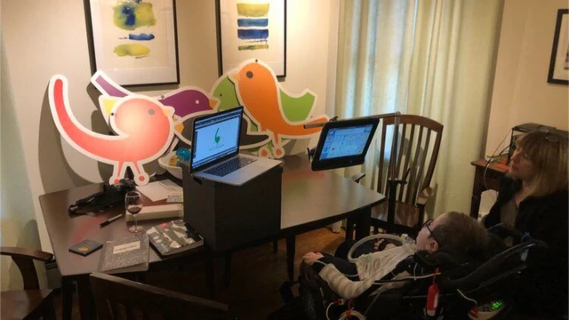 Alejandro sentado em cadeira na sala, olhando para monitores de computador
