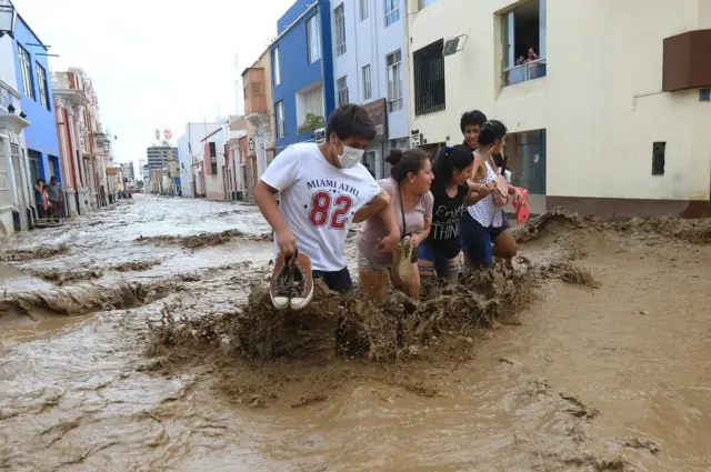 Personas tratando de cruzar una calle en medio del lodo.