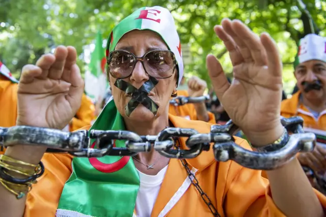 Les manifestants, en tenue assortie et avec des menottes factices, se tiennent côte à côte.