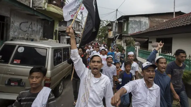 Warga berjalan membawa bendera merayakan keunggulan pasangan Anies-Sandi setelah keluar hasil hitung cepat.