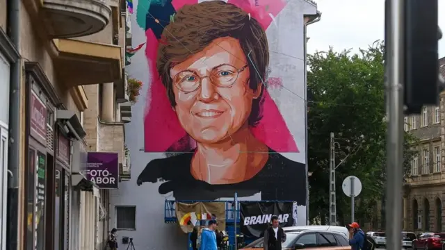 Mural na lateral1x freebetum prédio mostra o rosto da cientista Katalin Kariko, uma mulher branca1x freebetóculos e cabelo curto