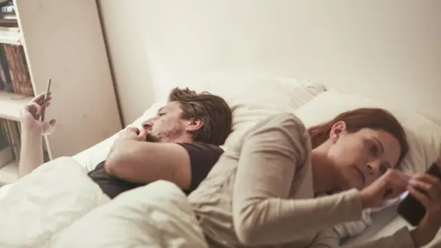 Pareja con sus teléfonos en cama.