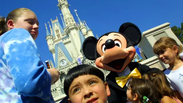 niños sonríen al lado de Mickey mouse y en el fondo el castillo Disney