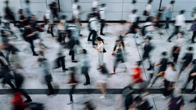 Uma jovem mulhervbet depósito mínimofoco nítido, usando smartphone, cercada por passageiros embaçados, correndovbet depósito mínimouma estação subterrânea durante os horáriosvbet depósito mínimopico