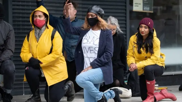 Cerca de cinco pessoas agasalhadas e ajoelhadas na rua