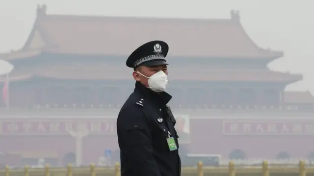 A security officer wearing a mask stands at the Tiananmen Square in haze