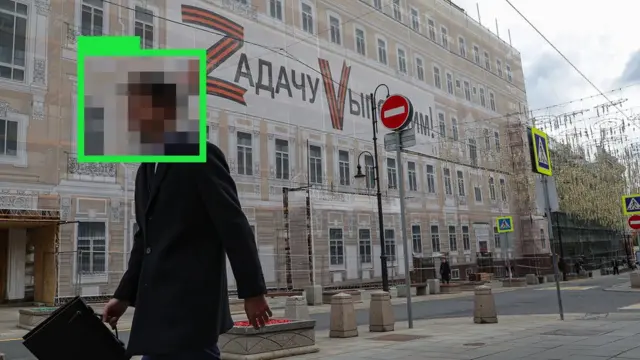 Moskva. Neopoznavaemый čelovek idet mimo zdaniя s propagandistskim transparantom