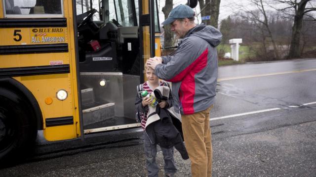 Pai e filho diante de ônibus escolar