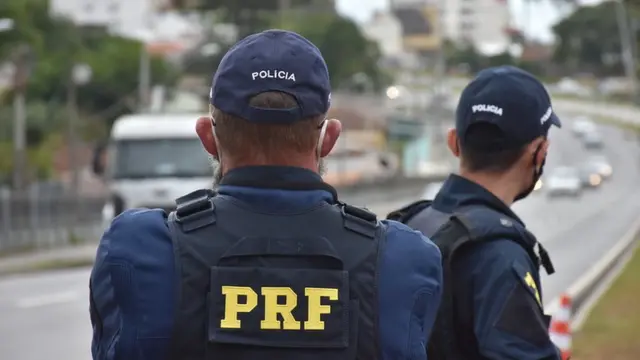 Dois agentes da PRF, identificados por coletes, olham para estrada