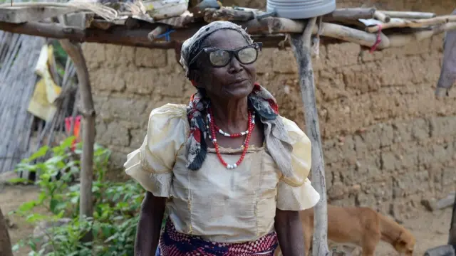 Amina Sarki, a 98-year old woman living in the north of Nigeria standing in front of a mud wall