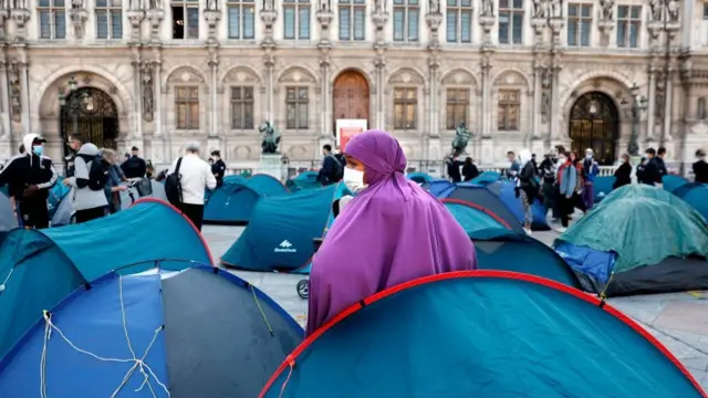 A woman with a mask stands as migrants are evacuated by police in front of the town hall of Paris, on September 1, 2020