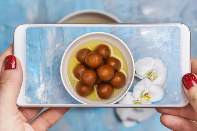 Žena fotografiše porciju gulab jamuna