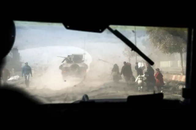 موكب من العربات المدرعة يمر إلى جوار عراقيين في شرقي مدينة الموصل.