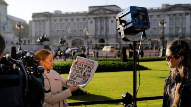 Mulher com jornal sobre discurso de membros da família real