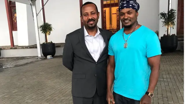 ጠቅላይ ሚኒስትር ዐቢይና ብሩክ አምዱ በአጤ ሚኒሊክ የግብር አዳራሽ ፊት ለፊት