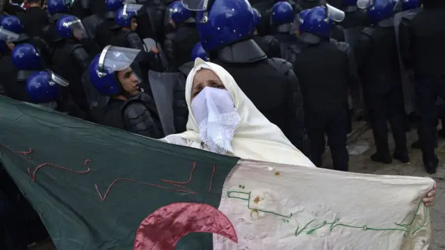 Mwanamke wa Algeria akiwa ameshikilia bendera ya taifa karibu na vikosi vya usalama vilivyozingira waandamanaji wakati wa maandamano ya kupinga mfumo wa utawala nchini humo katika mji mkuu wa Algeria, Algiers Jumatano tarehe 10 Aprili 2019