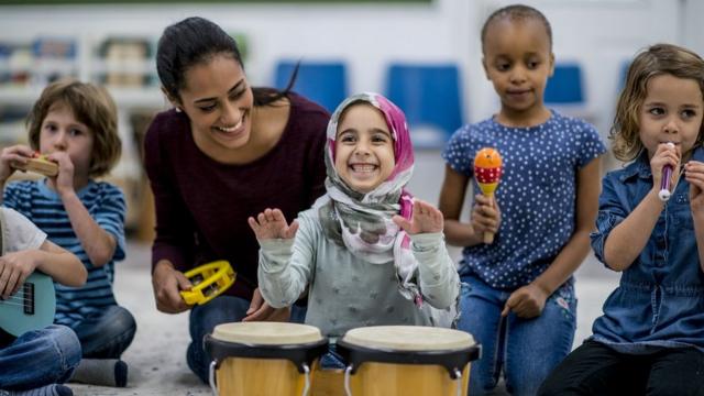 A multi-ethnic group of young school children are indoors in their classroom, playing instruments.