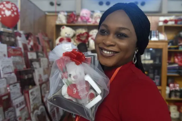 A woman smiles as she holds Valentine's Day gifts in a shop in Lagos' main airport on 13 February 2019. Supermarkets and shops stockpiled with Valentine's Day flowers and cards across the country are recording low sales because people are preoccupied with upcoming elections due on 16 February,
