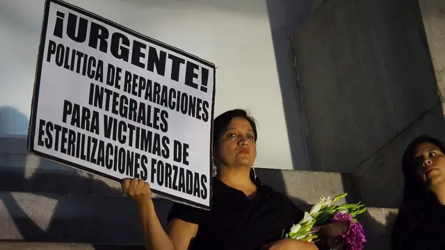 Mujer con una pancarta que reza "urgente, política de reparaciones integrales para víctimsa de esterilizaciones forzosas"