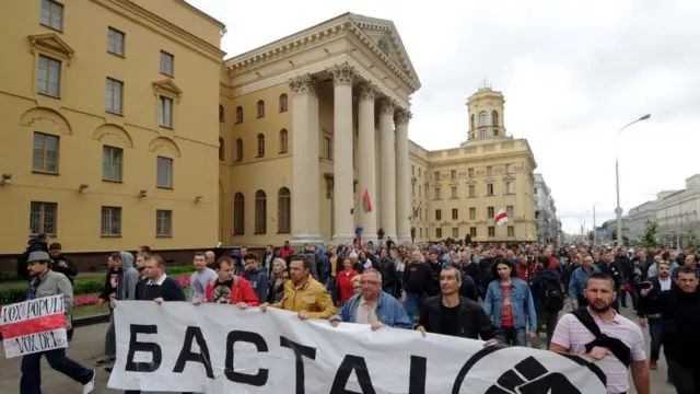 Grupo de manifestantes caminha com cartazes e faixas em frente ao prédio da KGB
