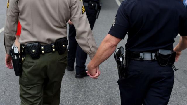 Un agente de policía y un agente de la oficina del alguacil caminan de la mano durante el desfile gay de Los Ángeles, junio de 2016