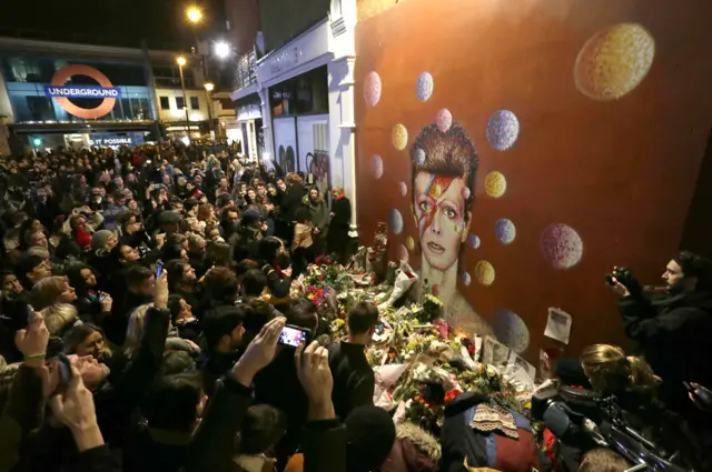 People gather at a mural of singer David Bowie by artist Jimmy C, in Brixton, south London.伦敦南部，民众在一幅由吉米·C创作的大卫·鲍伊壁画前致敬