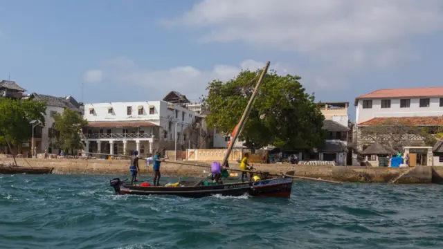 Barco no mar, com cidade ao fundo e homens a bordo