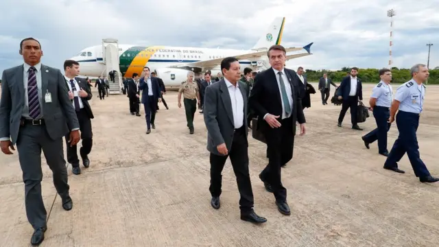 Mourão e Bolsonaro caminhamapostar nos jogos do brasileiraopista rodeados por seguranças e assessores, com avião no planoapostar nos jogos do brasileiraofundo