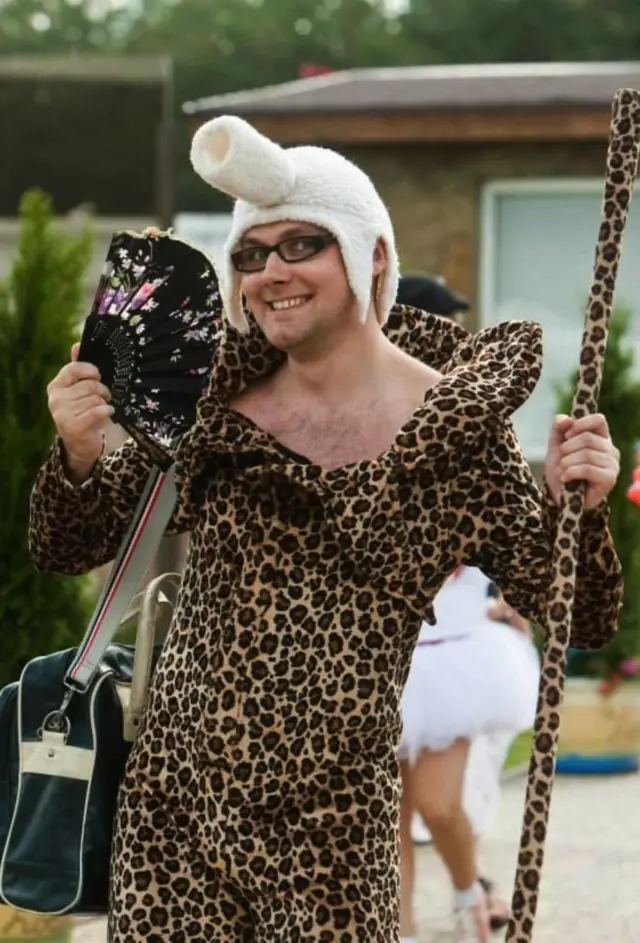 Vitaliy Kulko wearing a leopard skin onesie, holding a staff and wearing a hat with a tank-like turret