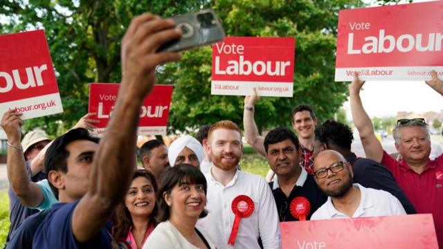 A Labour party activist takes a picture of Danny Beales (centre), Labour candidate for the Uxbridge and South Ruislip constituency, during a rally on Long Lane in Uxbridge, west London, where a by-election has been triggered by the resignation of former prime minister Boris Johnson. Picture date: Saturday June 10, 2023.
