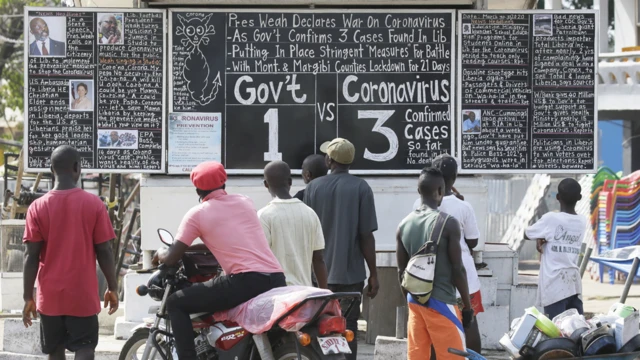 People reading a blackboard news board in Monrovia, Liberia - Monday 30 March 2020