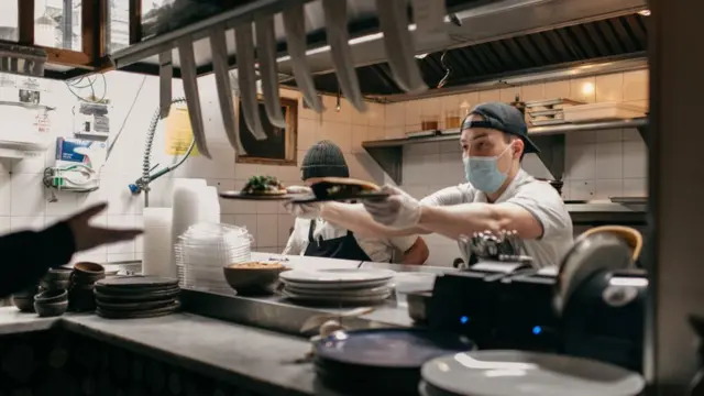Masked kitchen workers pass finished plates of food to a server at Claro restaurant on February 12, 2021 in New York City. New rules allow restaurants, bars, and cafes to reopen at 25% capacity due to the ongoing coronavirus pandemic