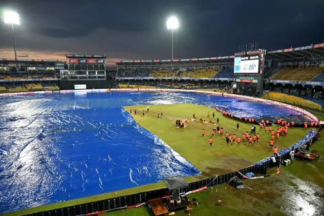 Ground staff cover the pitch after rain stopped play during the Asia Cup 2023 super four one-day international (ODI) cricket match between India and Pakistan at the R. Premadasa Stadium in Colombo on September 10, 2023