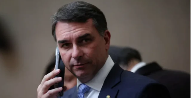 Foto mostra Flávio Bolsonaro usando terno e falando ao telefone celular.